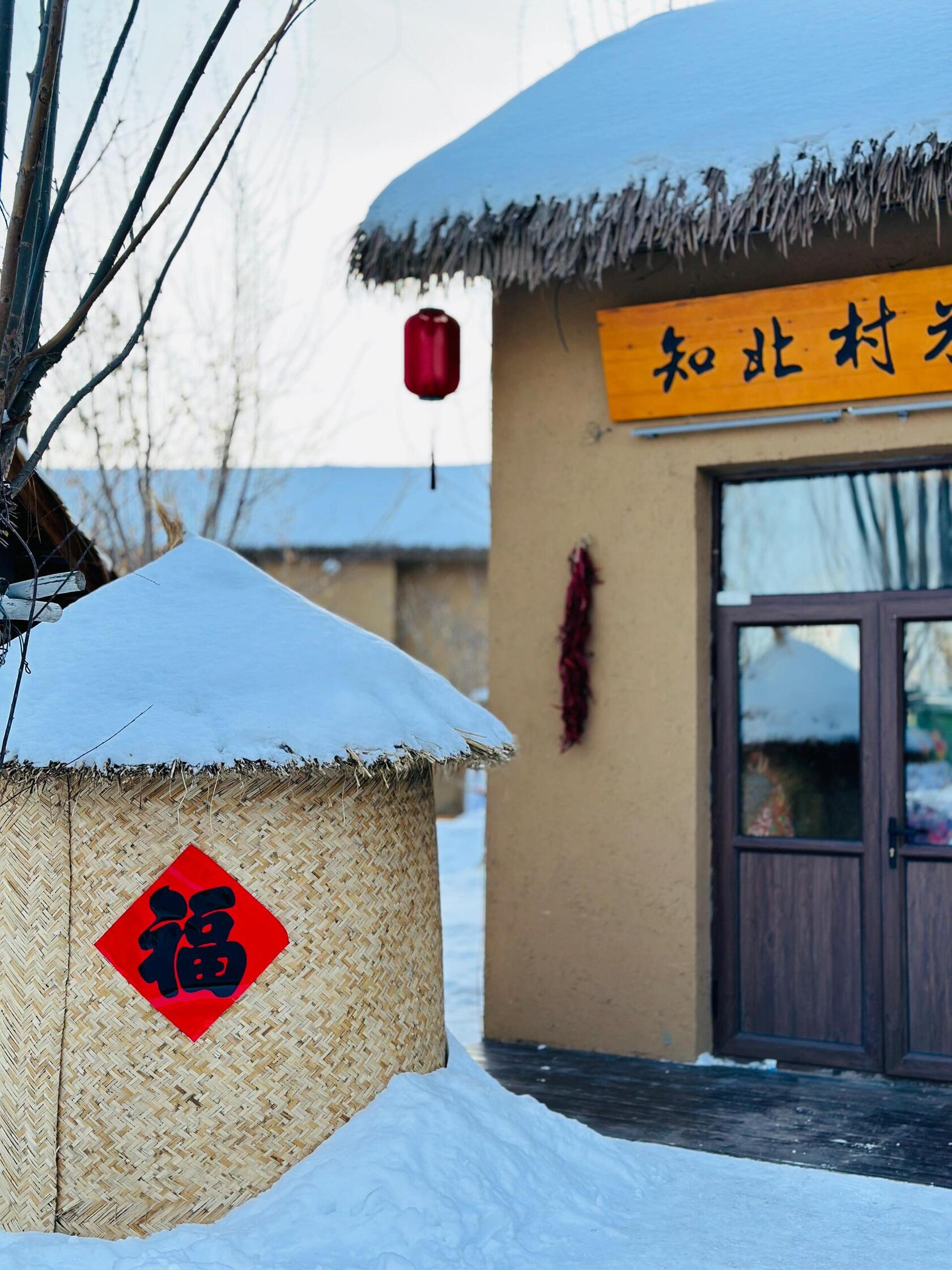 A snow-covered traditional village entrance with a 'Zhi Bei Cun' sign, showcasing a charming Northeast China winter village.