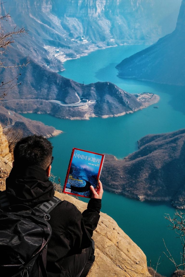 A person sitting at the edge of a cliff overlooking a scenic valley with a national geographic magazine, embodying the spirit of Shanxi Taihang Exploration.