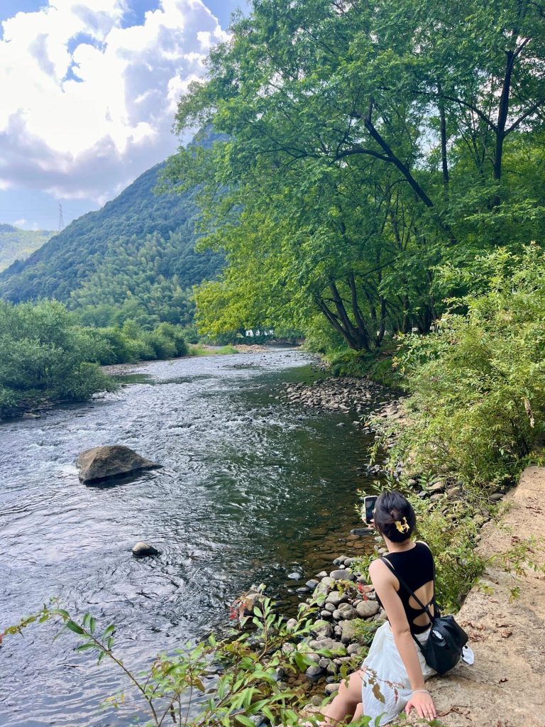A woman taking photos by a tranquil river, part of her Eastern China Exploration.