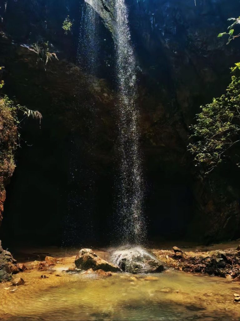 A slender waterfall cascading over rocks in a lush, green forest, a tranquil spot in this Guangdong Nature Adventure.