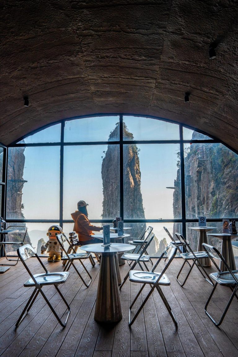 Interior of a modern cliffside cafe with panoramic views of misty mountains, a breathtaking Karst Landscape Wonders vista.